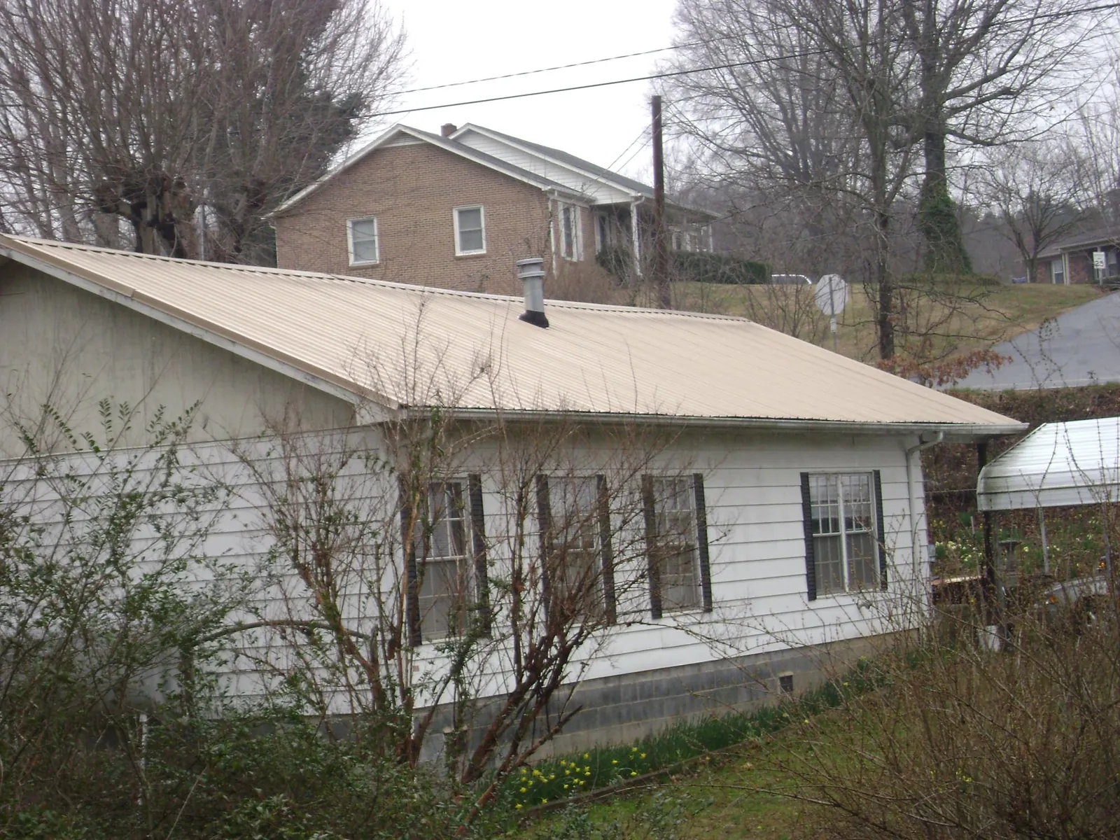 Tan metal roof on a white sided house set into a hillside — Commercial Roofing by Roofing Brothers in Dixie