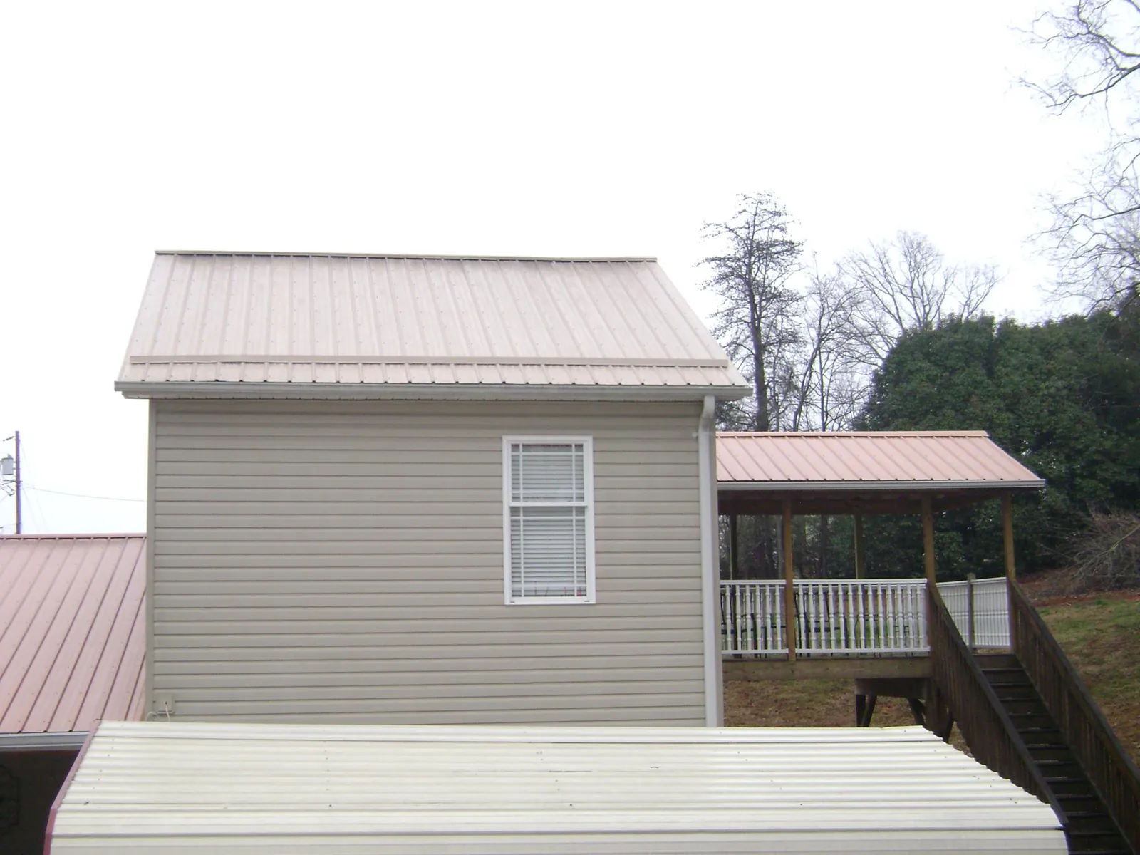 Tan metal roofs on a two story addition and attached porch, from a Roof Replacement job in Dixie